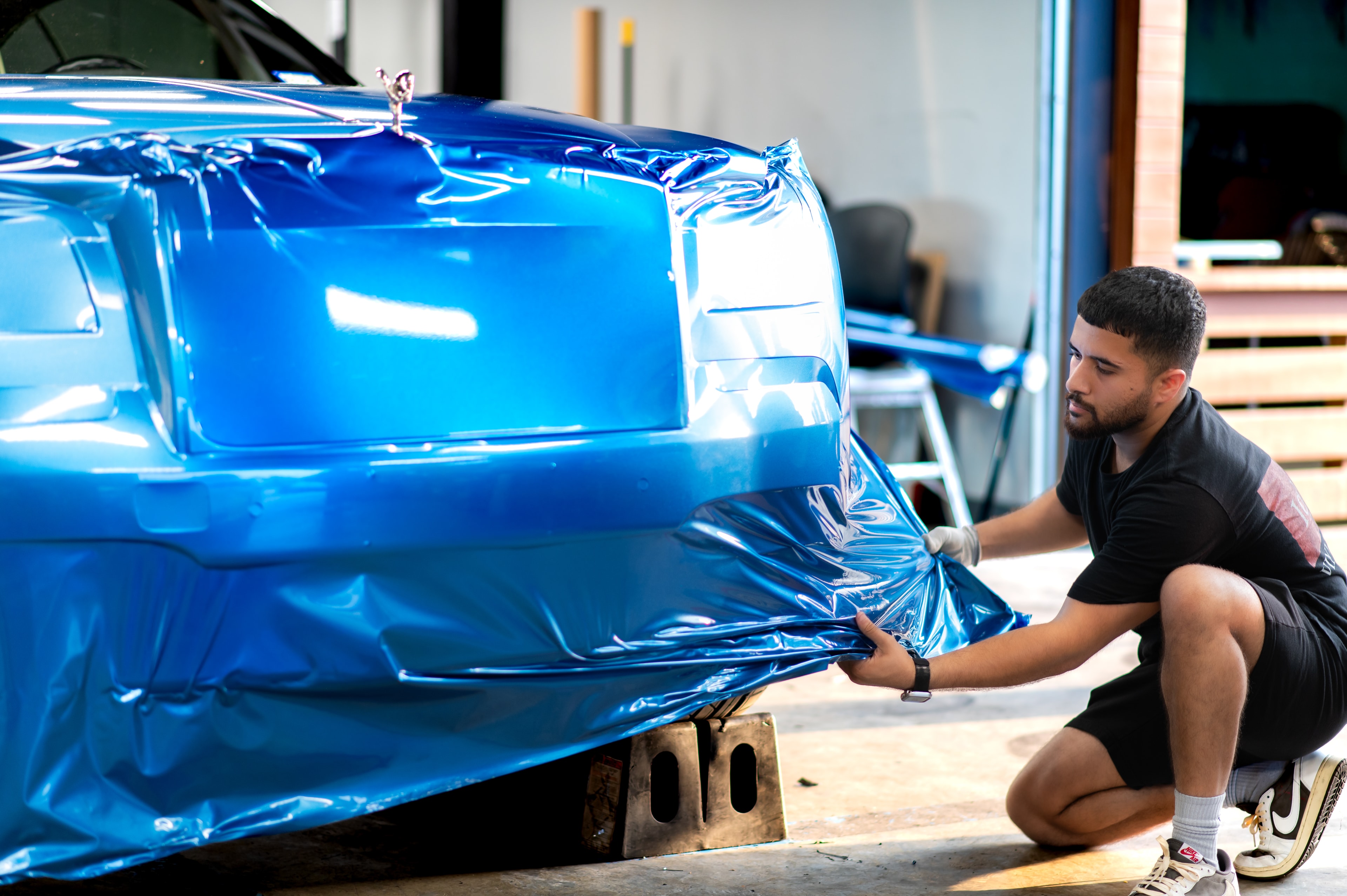 Installer hand-laying a blue metallic wrap in the Houston studio