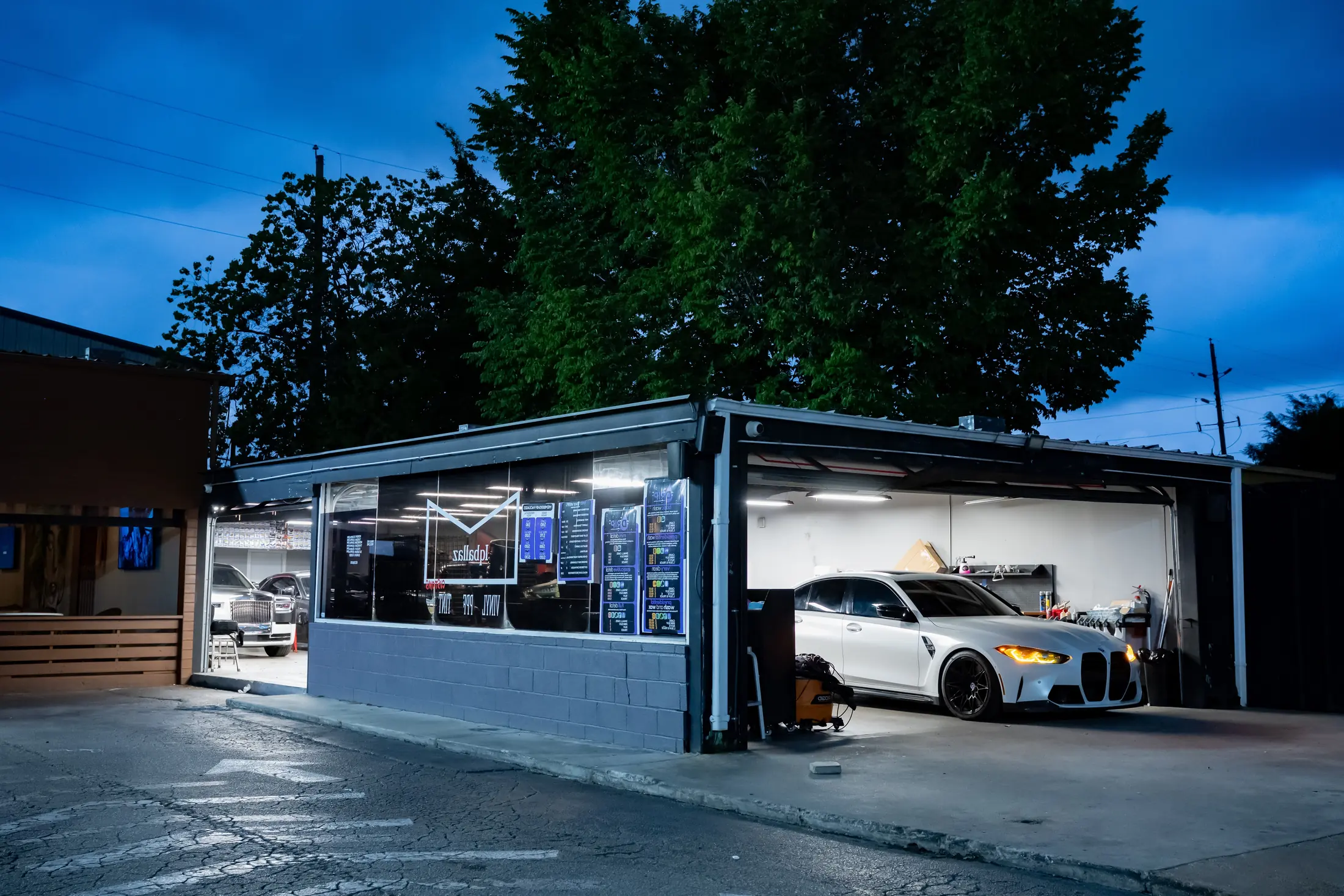Iqballaz Customs shop at dusk, a wrapped BMW M4 in the open bay